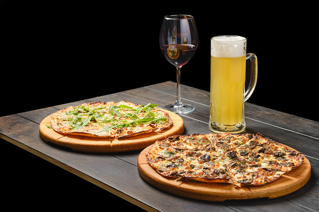 2 pizzas sur une table noire près d'un verre de bière et de vin