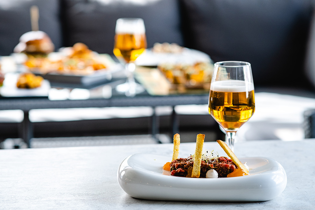 tartare servi dans une assiette blanche gastronomique près d'un verre de bière de dégustation haut de gamme