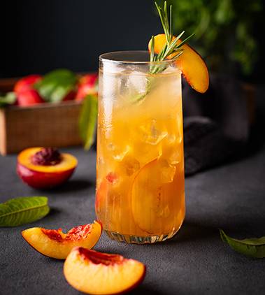 thé froid à la pêche dans un verre frais et des morceaux de fruits sur un fond noir